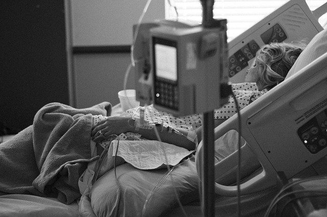 A woman in a hospital bed rests after a procedure, preparing for a long recovery